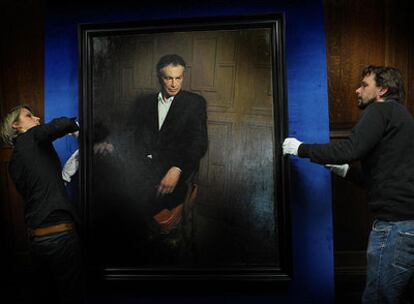 Dos operarios transportan el cuadro de Tony Blair.
