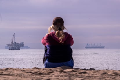 Una mujer mira hacia el océano en California; al fondo, una plataforma petrolífera y un buque.