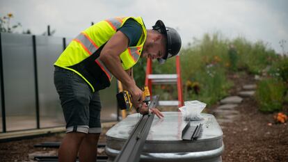 Trabajador taladrando puerta de aluminio de un invernadero dentro de una granja.