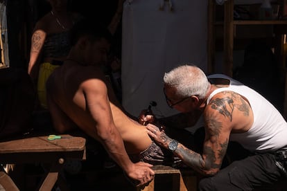 Un tatuador ex convicto realiza un diseño en el abdomen de Keylerth, un vecino migrante del campamento.