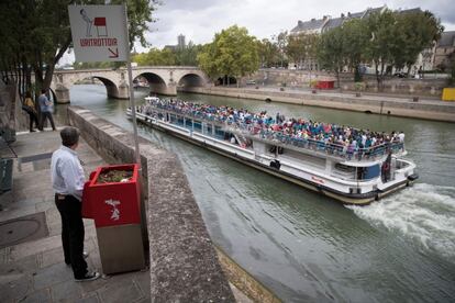 Un hombre se para frente a un urinario público "uritrottoir", en la isla de Saint-Louis en París, frente a una lancha turística.