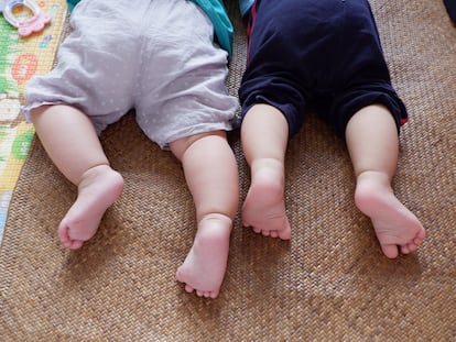 Dos bebés tumbados juntos en una alfombra.