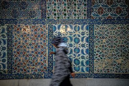 Una mujer camina al lado de una pared de azulejos tradicionales en la mezquita de Eyup Sultan en Estambul, Turquía.