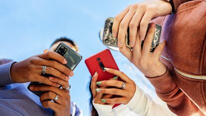 Tres jóvenes usando teléfonos móviles al aire libre.