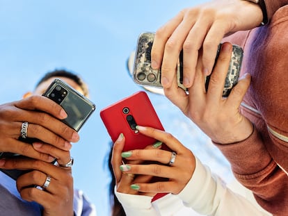 Tres jóvenes usando teléfonos móviles al aire libre.