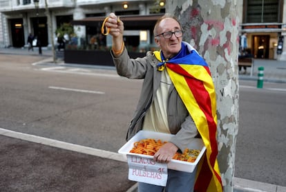 Un hombre, con una 'estelada' atada a su espalda, vende lazos amarillos y pulseras con la bandera catalana, antes del comienzo de una manifestación en Barcelona.