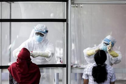 Profesionales de la salud recogen muestras a través de una pared de plexiglás durante una prueba de la covid-19 en Medan (Indonesia).