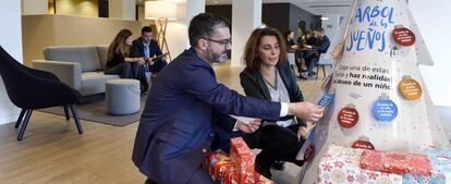 Dos empleados de CaixaBank colocan regalos en el Árbol de los Sueños de una oficina de la entidad financiera.