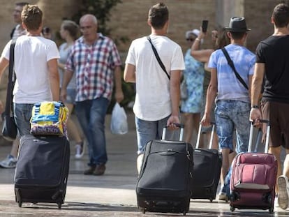 Cuatro j&oacute;venes turistas caminan con su maletas  por la plaza de la Virgen de Valencia. 