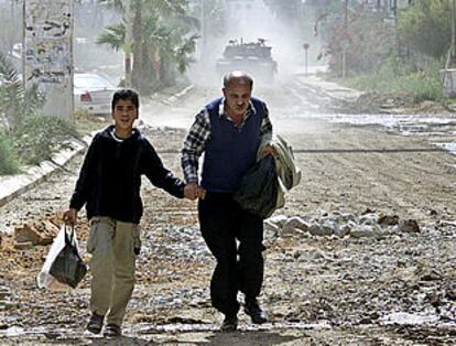 Un niño y un hombre palestinos corren por una calle de Yenín, en Cisjordania, ante un tanque israelí.