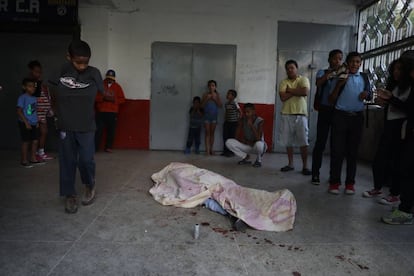 Personas pasan al lado del cuerpo de un manifestante que fue impactado por una bala durante las protestas de ayer, en Caracas