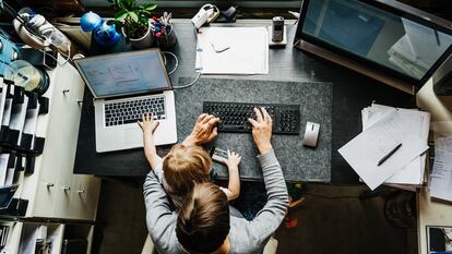 Uma mãe trabalha em 'home office' com sua filha no colo.