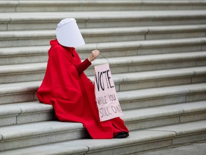 La activista Kelli Midgley disfrazada de El cuento de la criada, sostiene una pancarta en la que se lee