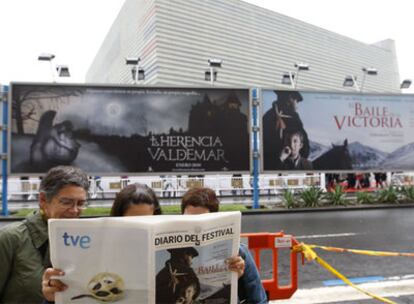 Varios asistentes al festival de cine miran el diario que se publica delante de la sede principal del certamen, el Kursaal