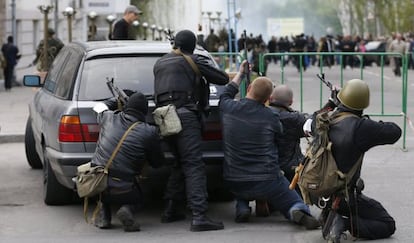 Um grupo de combatentes pró-russos se esconde atrás de um carro perto da sede da polícia de Luhansk, na Ucrânia.