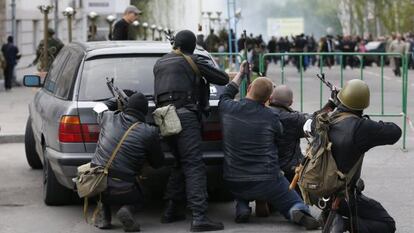 Um grupo de combatentes pró-russos se esconde atrás de um carro perto da sede da polícia de Luhansk, na Ucrânia.
