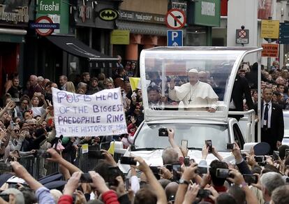 El Papa Francisco saluda a los fieles desde el Papamóvil, al lado del cual se puede ver una pancarta que lee: "El Papa es el jefe de la red de pedófilos más grande de la humanidad" el 25 de agosto de 2018, en Dublín. 