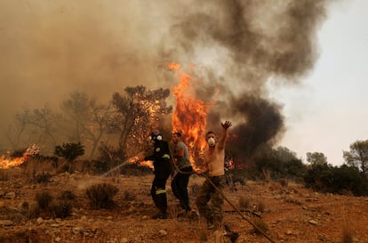 Men help a firefighter as they try to extinguish a wildfire burning near the village Vlyhada, near Athens, Greece, on July 19, 2023.