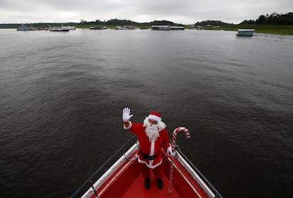 Santa Claus saluda a bordo de un barco antes de distribuir regalos a los niños que viven en las comunidades ribereñas del Amazonas, este sábado en Iranduba, Brasil.