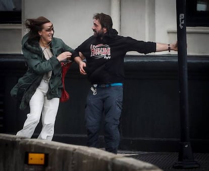 Dos viandantes se agarran a una farola para no caerse a consecuencia de las fuertes rachas de viento, este viernes, en San Sebastián.