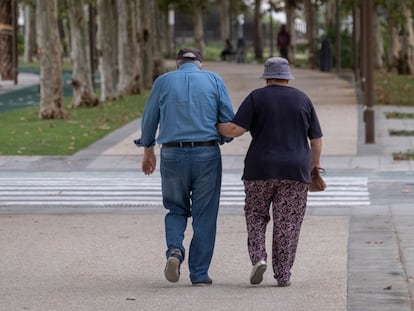 Dos personas mayores caminan por la calle agarradas del brazo.