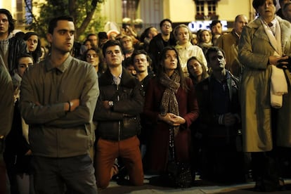 Un grupo de personas se arrodillan en la acera y rezan mirando cómo envuelven las llamas la catedral de Notre Dame en París.