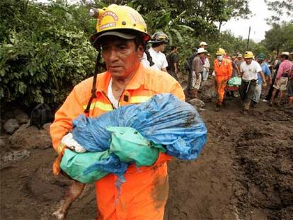 Un bombero lleva en brazos el cuerpo de un niño muerto en el desprendimiento de tierras en Panabaj.