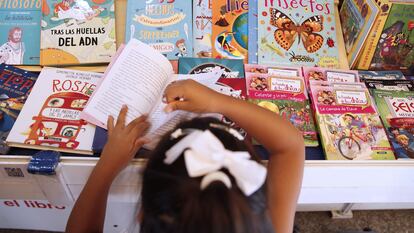 Una niña ojea un libro en una caseta de la Feria del Libro de Madrid.
