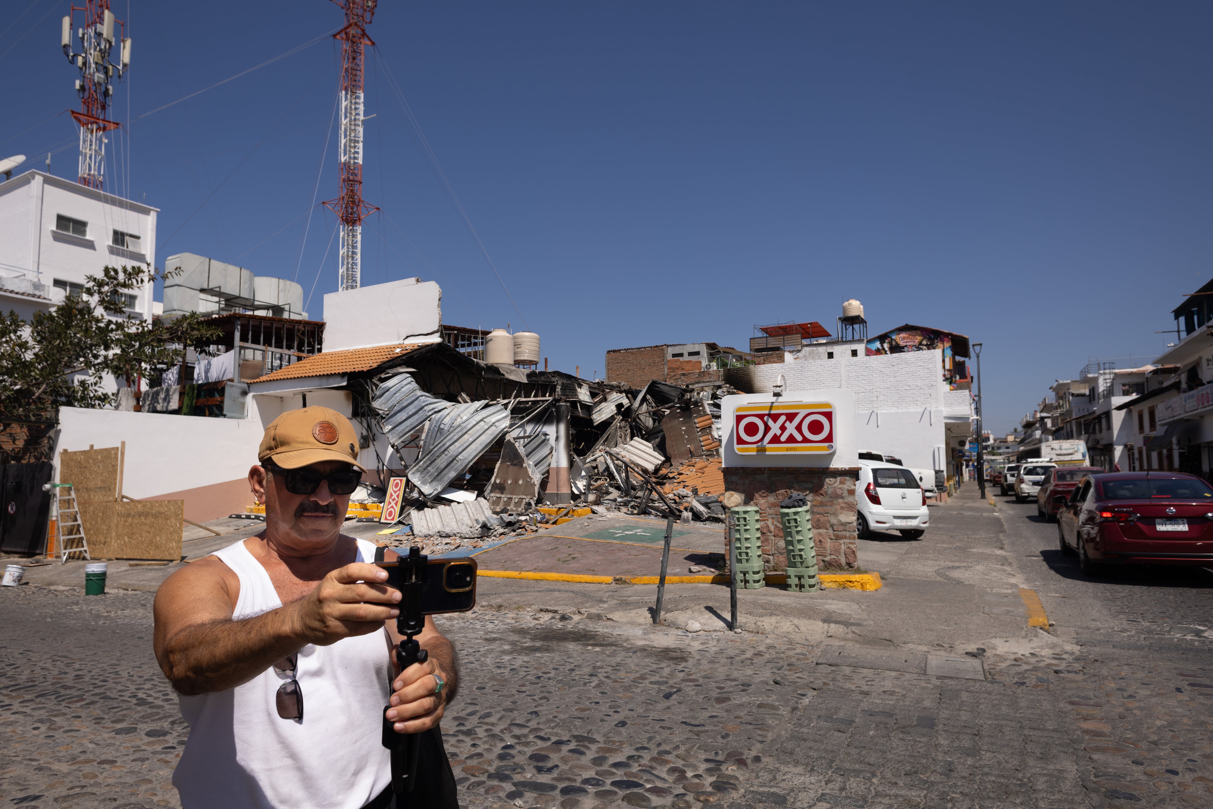 Un turista se toma una selfie frente a una tienda Oxxo quemada durante el operativo contra El Mencho.