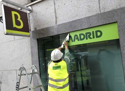 Un empleado retira un cartel de Caja Madrid de una oficina de Bankia.