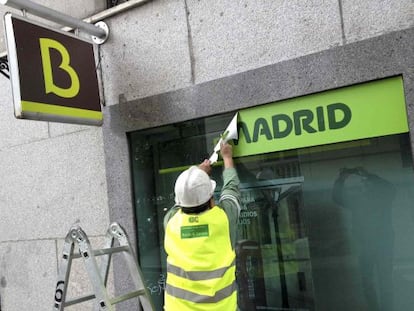 Un empleado retira un cartel de Caja Madrid de una oficina de Bankia.