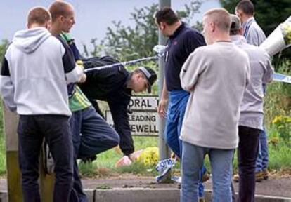 Un grupo de amigos recuerda al joven asesinado en Belfast mientras un policía coloca un ramo de flores traído por ellos en el lugar del crimen.