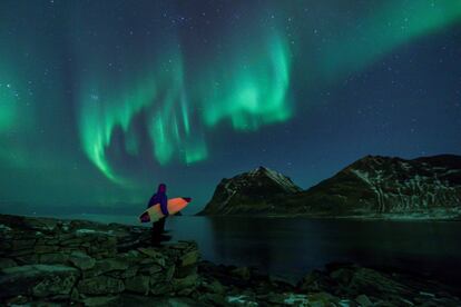 Um surfista sob uma aurora boreal em Utakleiv, Ilhas Lofoten (Noruega).