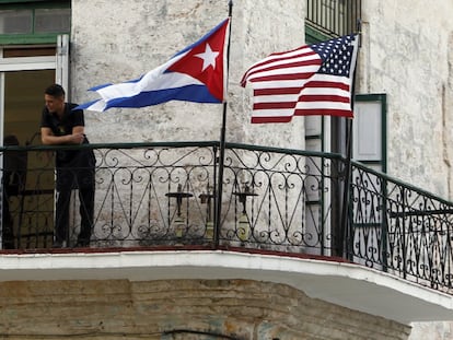 Dos jóvenes cubanos conversan junto a las banderas de Estados Unidos y Cuba, en La Habana