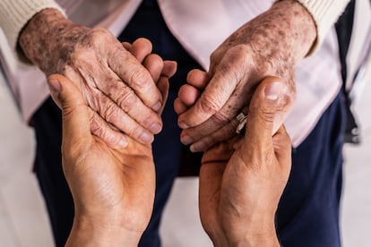 Eine Nahaufnahme der gefalteten Hände einer älteren Frau und ihrer Pflegekraft.