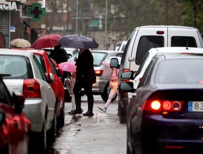 Peatones transitan entre los coches durante una mañana de lluvias en Madrid. 