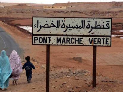 Dos mujeres y un niño pasan junto a un cartel donde se lee "Puente de la Marcha Verde".