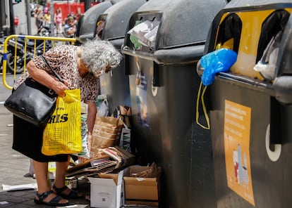 Una señora vacía una bolsa de reciclaje fuera del contenedor.