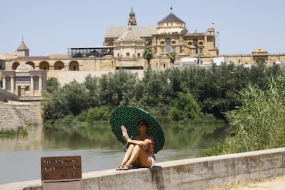 Una turista se protege del calor con un paraguas y un abanico a la orilla del río Guadalquivir, cerca de la catedral de Córdoba, este lunes. La Agencia Estatal de Meteorología (Aemet) alerta que la segunda ola de calor alcanzará o superará hasta el jueves los 44 grados.