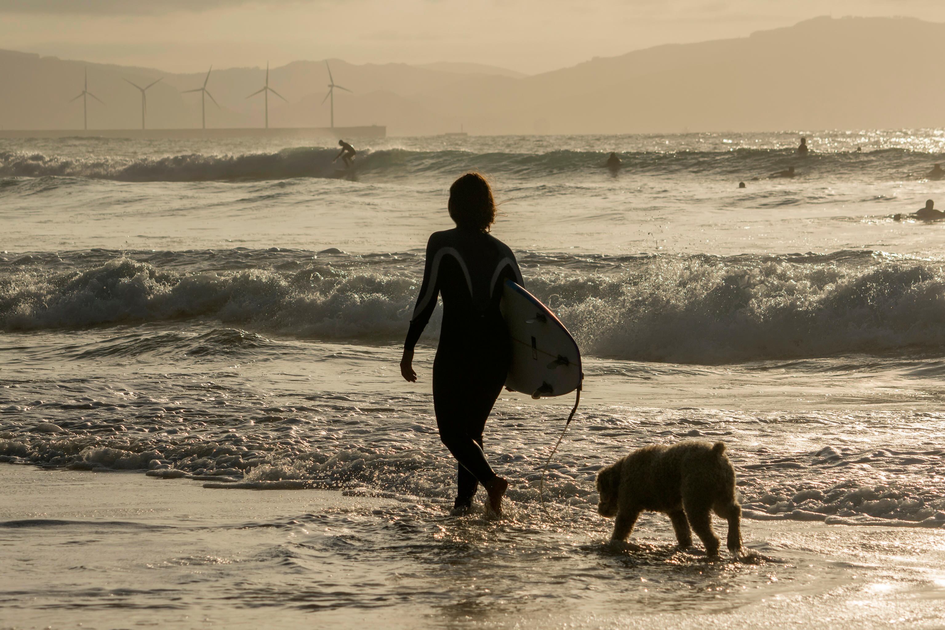 Una surfista, acompañada de su perro, en una playa bilbaína.