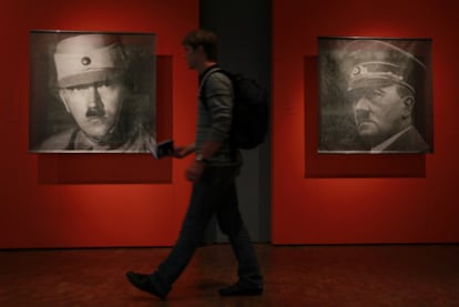 Un joven camina frente a dos retratos de Hitler expuestos en: <i>Hitler, la nación alemana y el crimen, </i>exposición inaugurada en Berlín el 15 de octubre de 2010. Abajo, uniformes del Führer.