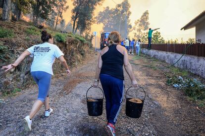 Una mujer lleva agua para ayudar a apagar las llamas en Oliveira De Azemeis, Portugal, este lunes. 