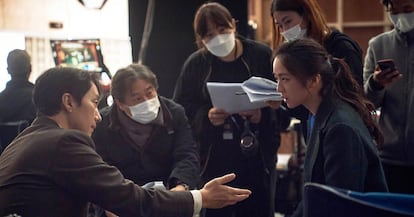 Park Chan-wook, kneeling and wearing a mask, on the set of 'Decision to Leave.'