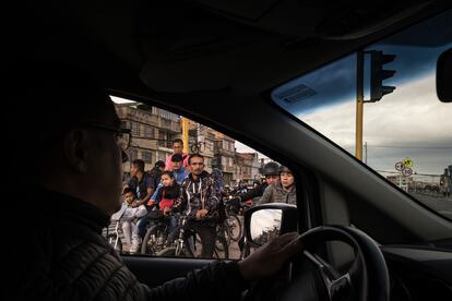 El conductor de un vehículo observa a los ciclistas que espera para cruzar una avenida, en Bogotá.