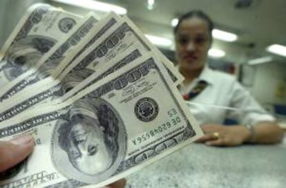 Un empleado bancario contando billetes de dólar ante un cliente en un banco. EFE/Archivo