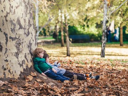 Tres niños reflexionan apoyados en un árbol.