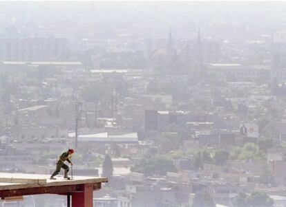 Un trabajador de la construcción en la parte superior de un edificio. Al fondo la nube contaminante