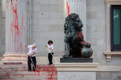 Dos operarias limpian el león del Congreso tras ser pintado por una protesta medioambientalista.