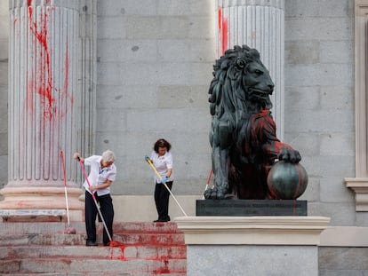 Dos operarias limpian el león del Congreso tras ser pintado por una protesta medioambientalista.