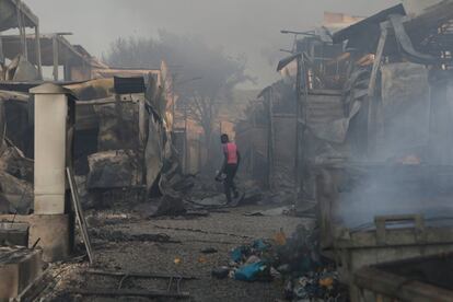 Un migrante camina entre los restos de viviendas improvisadas calcinadas por el fuego.